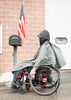 Person in a wheelchair wearing a raincoat in front of a brick building with an American flag.