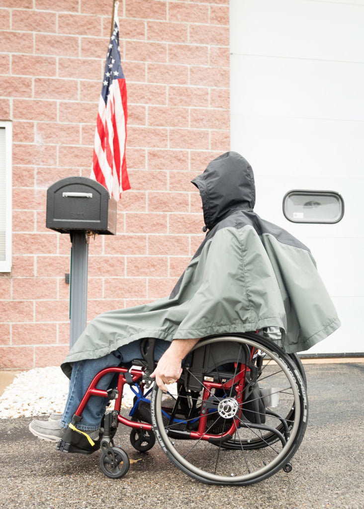 Person in a wheelchair wearing a raincoat in front of a brick building with an American flag.
