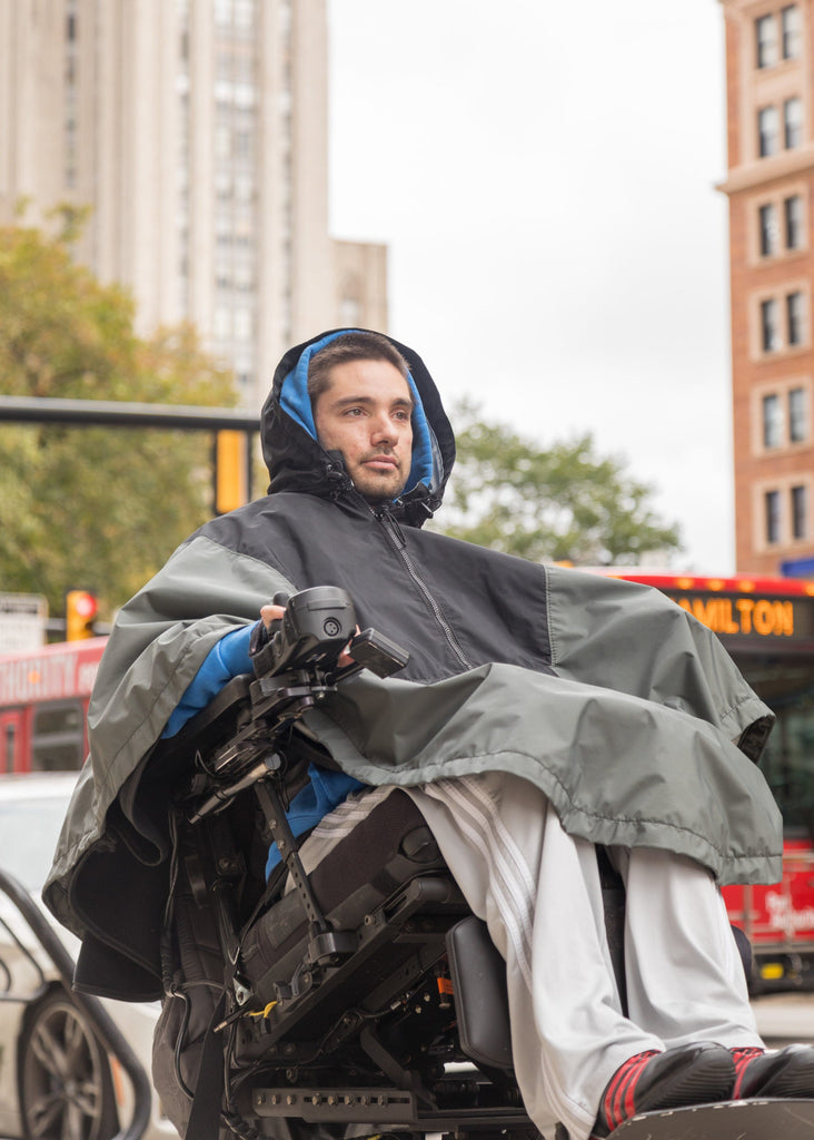 Person using a wheelchair with a large gray hooded coat in an urban setting