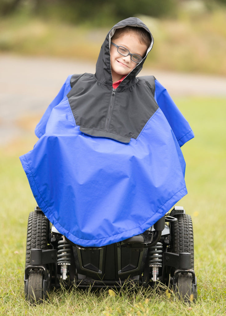 Child in a blue and gray poncho sitting in a mobility device outdoors.
