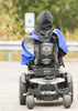Person using a mobility scooter on a road with a blurred background, wearing a blue wheelchair poncho.