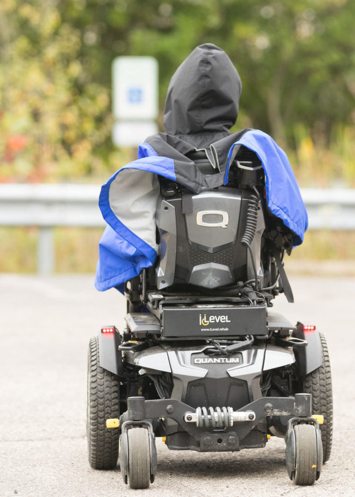 Person using a mobility scooter on a road with a blurred background, wearing a blue wheelchair poncho.