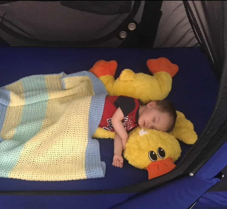 Toddler boy sleeping in The Safety Sleeper with a knit blanket and yellow duck stuffed animal.
